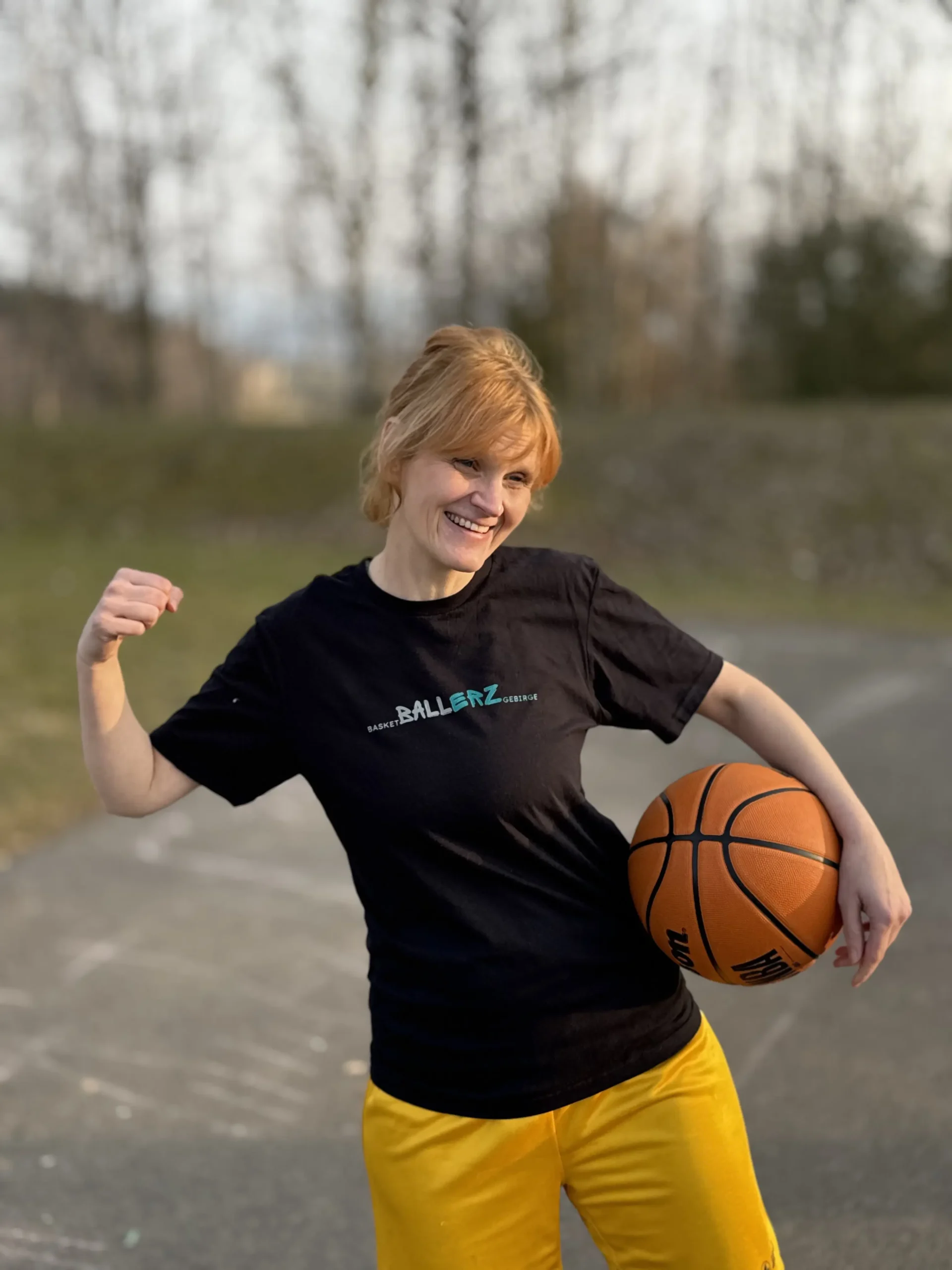 Eileen Prades, bekleidet in einem schwarzen T-Shirt mit der Aufschrift Ballerz. Unter einem Arm hält sie einen Basketball.